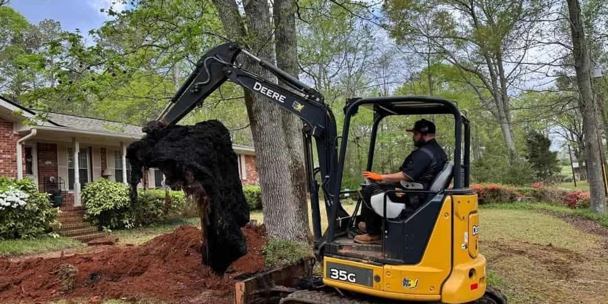Man operating a yellow John Deere excavator in a yard.