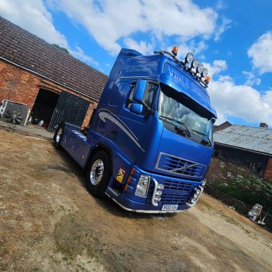 Blue Volvo semi-truck parked near rustic buildings.
