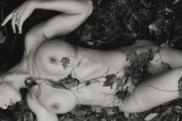 Nude woman laying in the forest on leaves with her dog sitting by her.