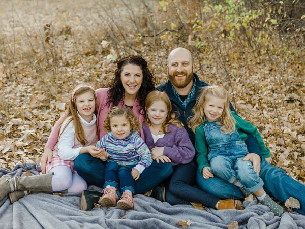 A happy family of six sitting on a blanket in an autumn forest.