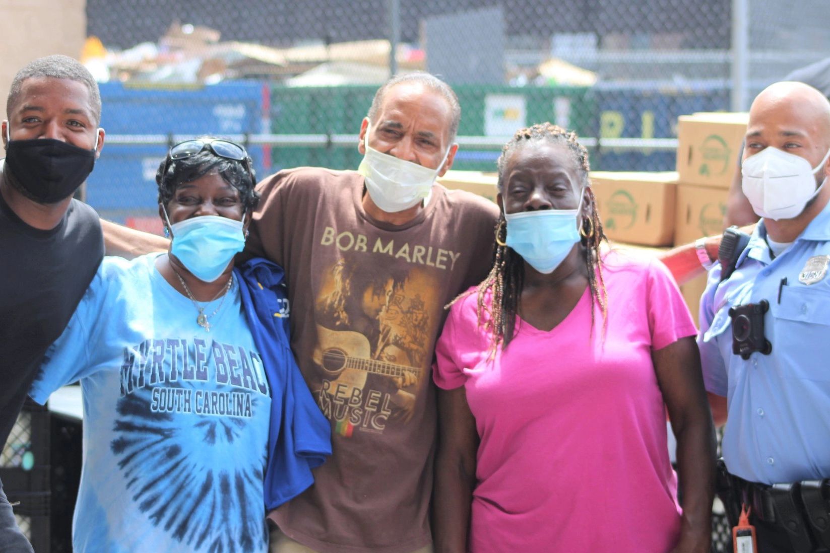 Three black men and two black women stand together and smile while wearing protective face masks