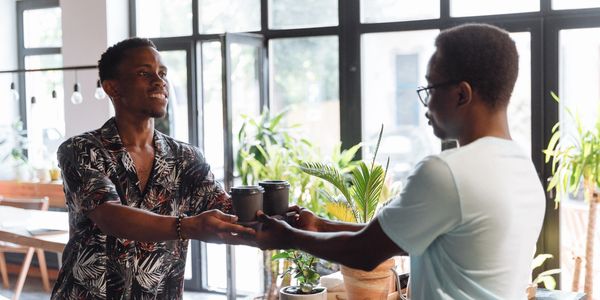 two black men exchange coffee at a cafe
