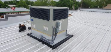 Commercial rooftop HVAC unit on a metal roof with a tool bag nearby.
