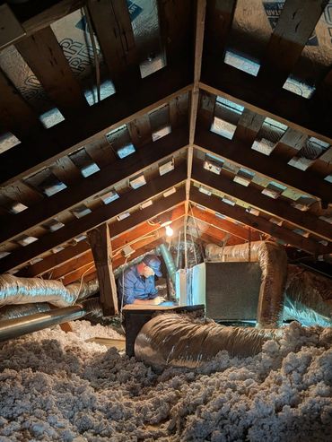 Technician inspecting HVAC system in an attic filled with insulation.