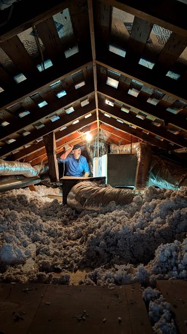 Man inspecting attic insulation and ductwork under dim light.