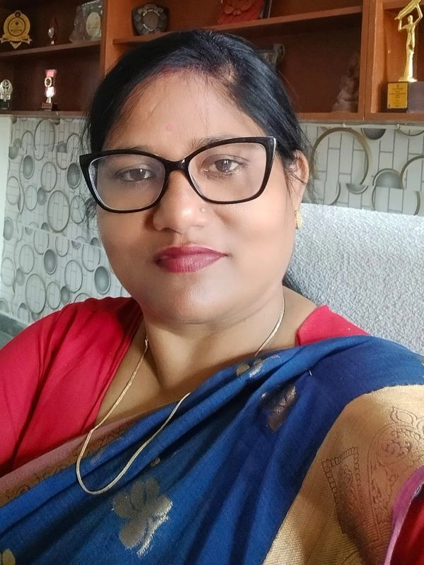 Woman wearing glasses and a blue and gold saree, smiling gently.