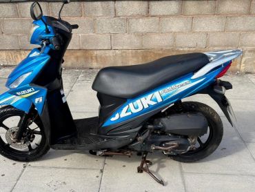Blue Suzuki Address scooter parked on sidewalk.
