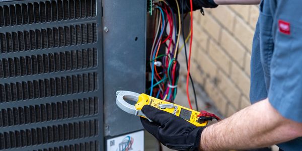 HVAC technician testing an air conditioner capacitor with a multimeter during an AC repair service.