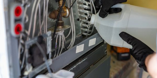 Technician pouring water into evaporator drain pan to test AC condensate drainage.