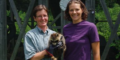 JoAnn standing with another woman and holding a raccoon