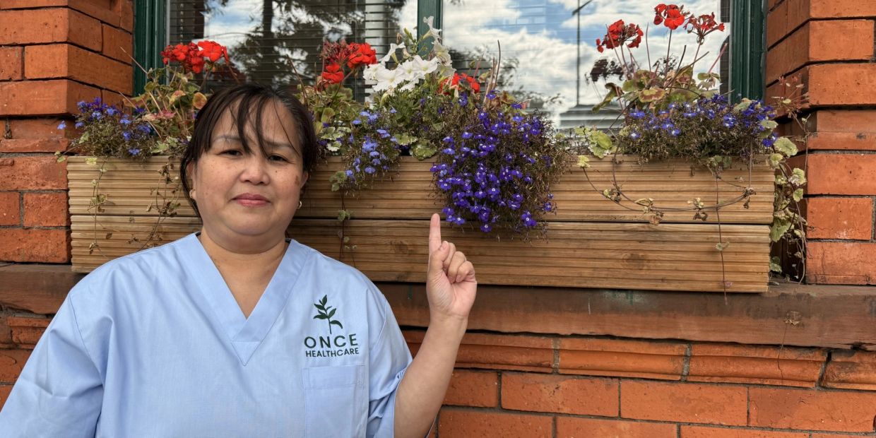 Healthcare worker pointing at colorful flowers on a brick wall.