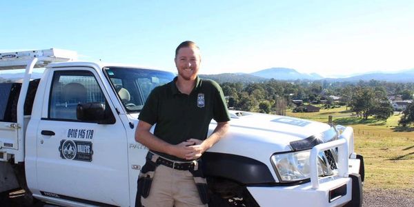 Man standing in front of work vehicle, background of green hilly land and mountains in far distance