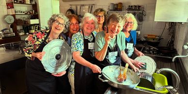 A group of joyful older women in aprons cleaning kitchen utensils together.
