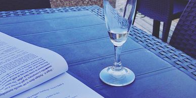 A glass and an open book on a blue table outdoors.