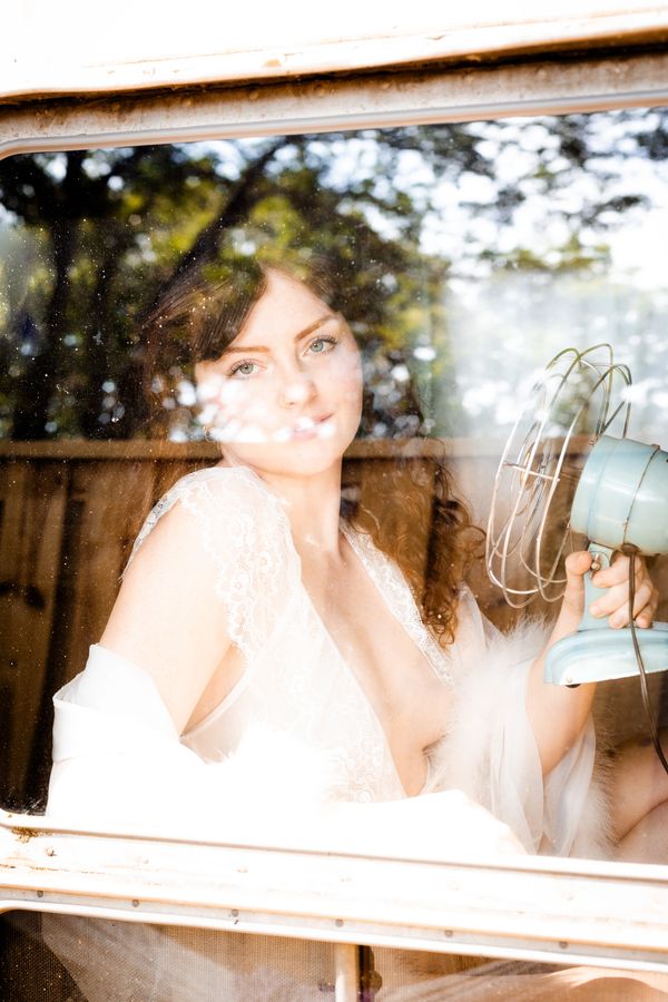 Woman in white lace holding a vintage fan, seen through a bright window.