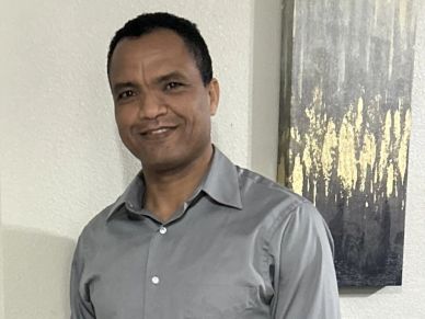 A man smiling, wearing a grey shirt.