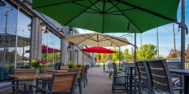 Outdoor seating area with colorful umbrellas and wooden tables by a building.