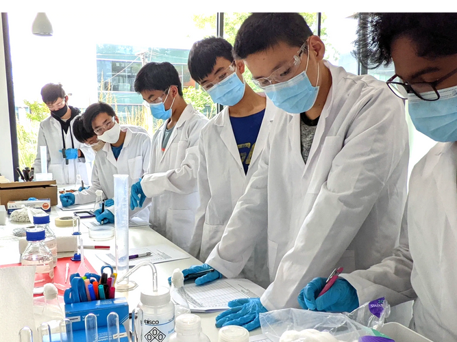 Group of Pre-VCE Chemistry students wearing lab coats and gloves at a chemistry workbench