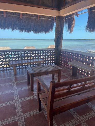 Wooden seating area overlooking a calm waterfront with thatched roof shade.