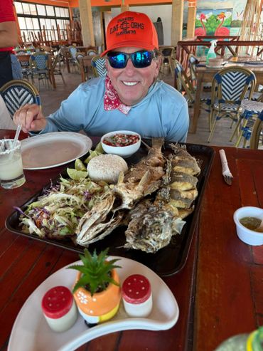 A man smiling behind a large tray of grilled fish, rice, and salad in a restaurant.