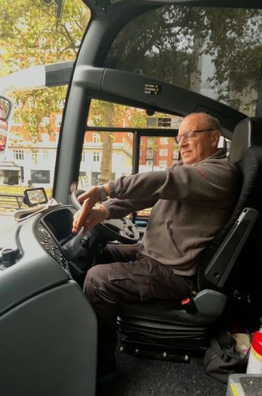 An elderly man driving a bus with focus and care.