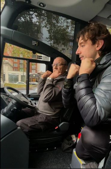 Two men sitting in a vehicle cabin, playfully posing with fists near their faces.