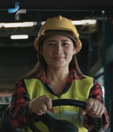 Female construction worker wearing helmet and safety vest, smiling while steering.