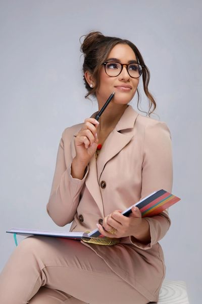 Thoughtful woman in glasses holding a pen and notebook.