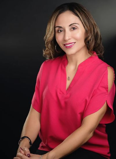 Confident woman in a bright pink blouse smiling against a dark background.