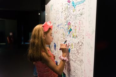 Момиче рисува върху голяма интерактивна стена за рисуване във Fantasy Не-Музеят.
