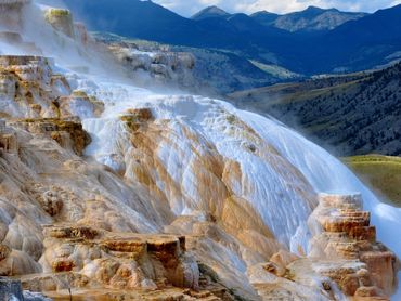 Steaming terraces of Mammoth Hot Springs against mountainous backdrop.