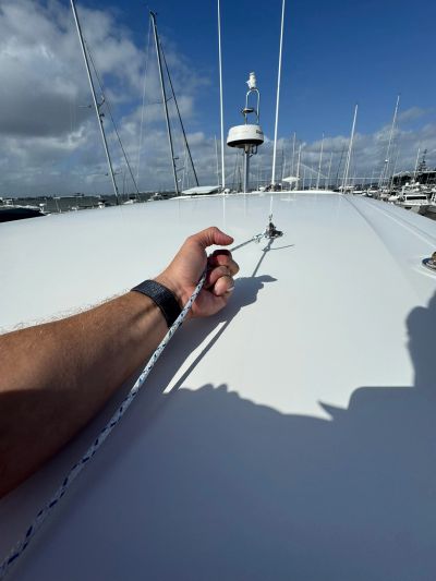 Hand holding a rope on a boat deck under a blue sky.