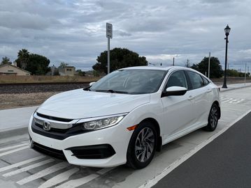 White Honda sedan parked on a street under a cloudy sky.