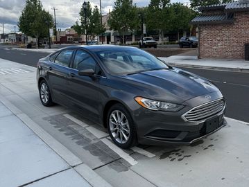 A gray Ford sedan parked on a city street under a cloudy sky.