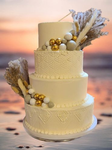 4 Tier Boho Wedding cake. All white with white accents. Gold, white and tan Balls with feathers.