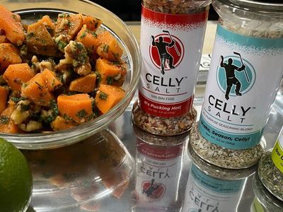 A bowl of seasoned sweet potatoes with Celly Salt seasoning bottles.