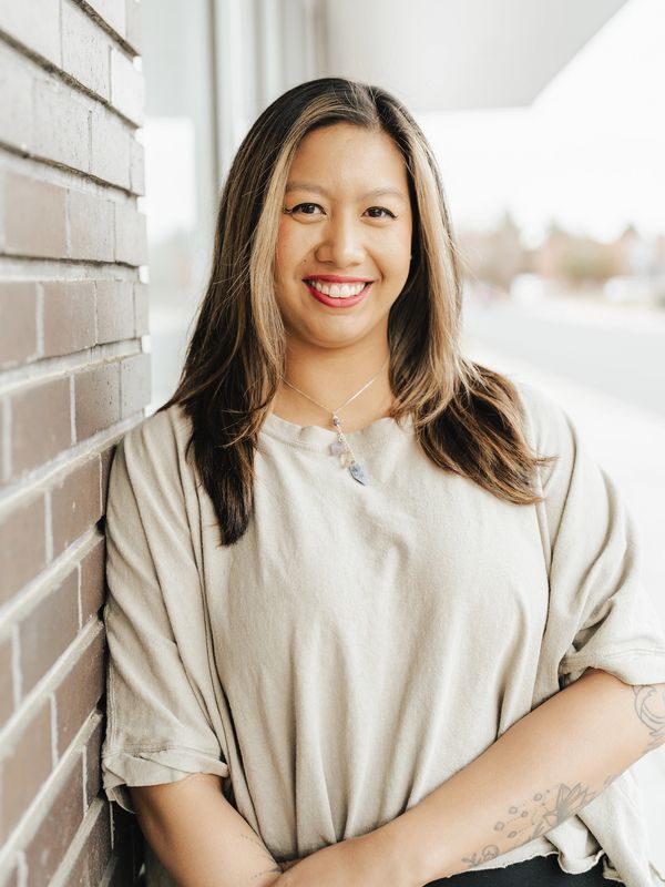 Smiling woman leaning against a brick wall.
