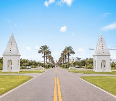 Palm tree-lined road flanked by white architectural towers under a clear blue sky.