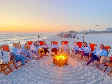Group of women sitting around a beach bonfire at sunset.