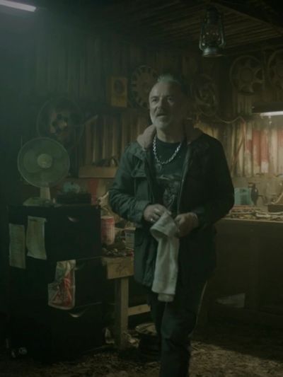 Man standing in a dimly lit, cluttered workshop.