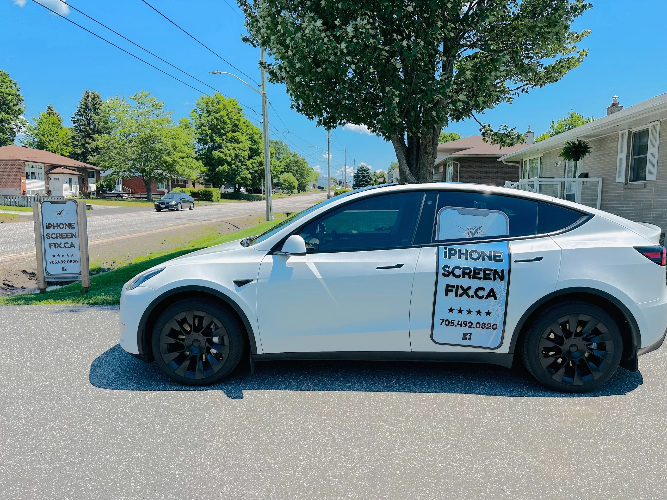 White Tesla with iPhone screen repair advertisement parked on a sunny suburban street.