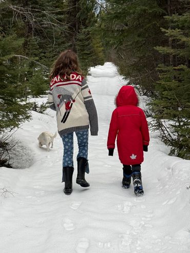 Two children and a dog walking on a snowy forest path.