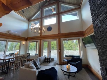 Bright living room with vaulted wood ceiling and large lake-view windows.