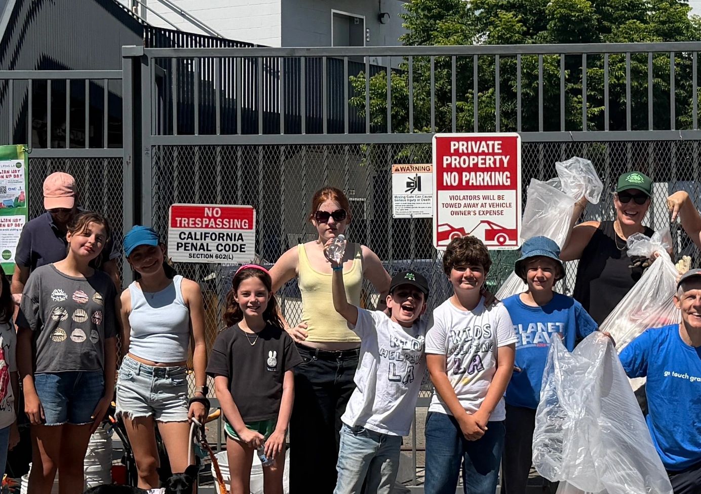 Group of kids and adults with bags and signs behind a gate.