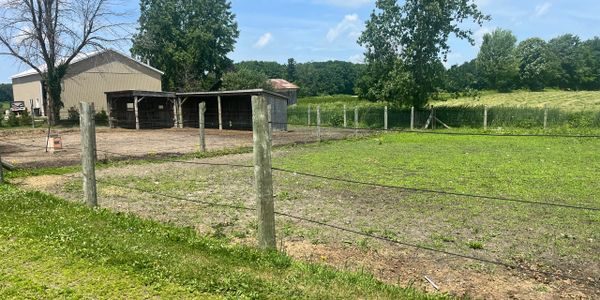 A fenced rural area with a barn and open fields under a clear sky.