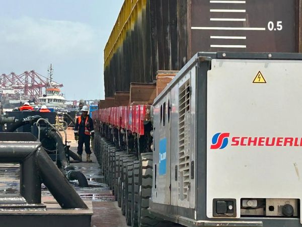 Workers operate heavy machinery and transport equipment at a busy industrial port.