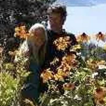 Couple hugging in front of a flower bed with the Okanagan lake in the background