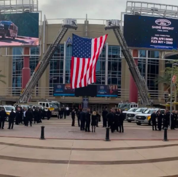 Large American flag displayed by fire trucks at event.