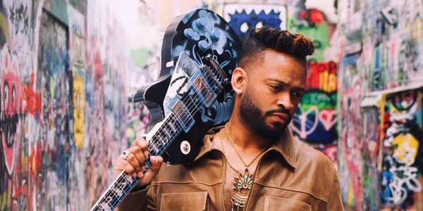 Man holding a guitar in a graffiti-covered alley.