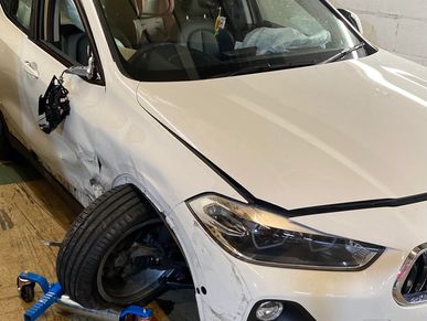 White car with severe damage to the front left side and missing side mirror.
